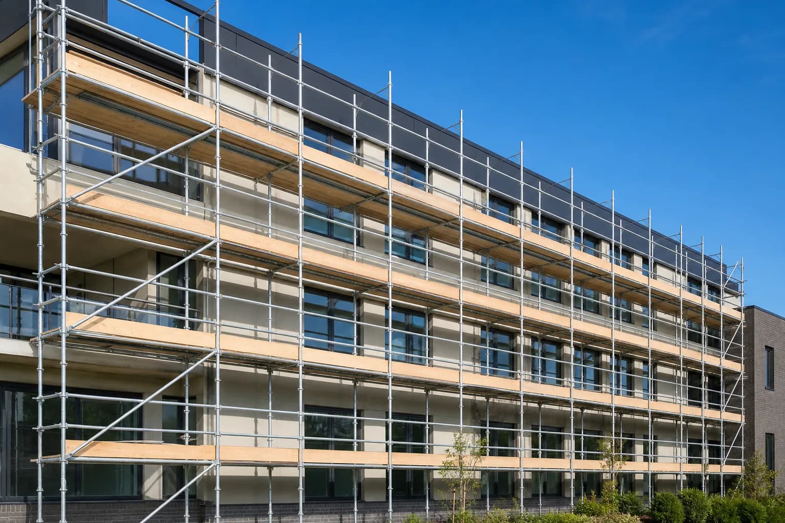 Scaffolding erected across the front of a modern multi-storey building under a clear blue sky